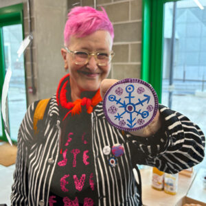 Artist Rachael House showing off a badge with one of her designs