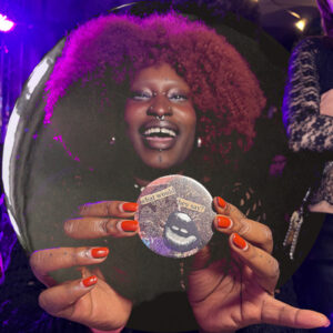 A smiling participant at Queer House Party showing off her badge
