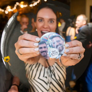 A smiling wedding guest showing off a badge showing the happy couple