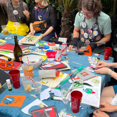 Ben and participants at an outdoor badge table covered in materials and drinks at Duckie