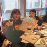 Three participants at Rich Mix at a colourfully cluttered badge table
