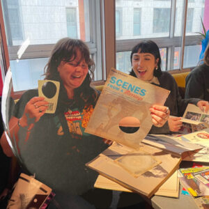 Three participants at Rich Mix at a colourfully cluttered badge table
